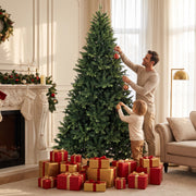 Man and child hanging baubles on the 7ft tree above a pile of red gifts