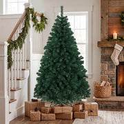 Green Christmas tree in a hallway by a staircase with garland and wrapped gifts around the stand
