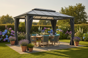 Grey aluminium hardtop gazebo with polycarbonate roof and dark grey privacy curtains on a stone patio in a British garden with outdoor dining setup at golden hour