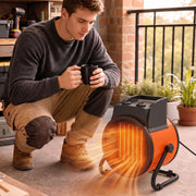 Man crouching on a balcony holding a mug beside the glowing industrial fan heater