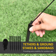 Hand pushing a ground stake into grass beside spare stakes and tethers