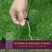 Hand pressing a ground stake into grass next to spare stakes and tethers