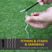 Hand holding a metal ground stake on grass with tethers and spare stakes