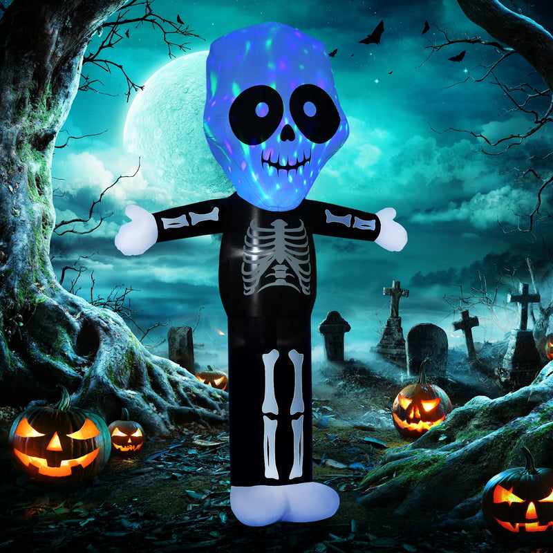 Inflatable skeleton lit up at night beside a graveyard scene and carved pumpkins
