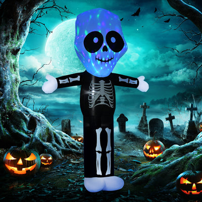 Inflatable skeleton lit up at night beside a graveyard scene and carved pumpkins