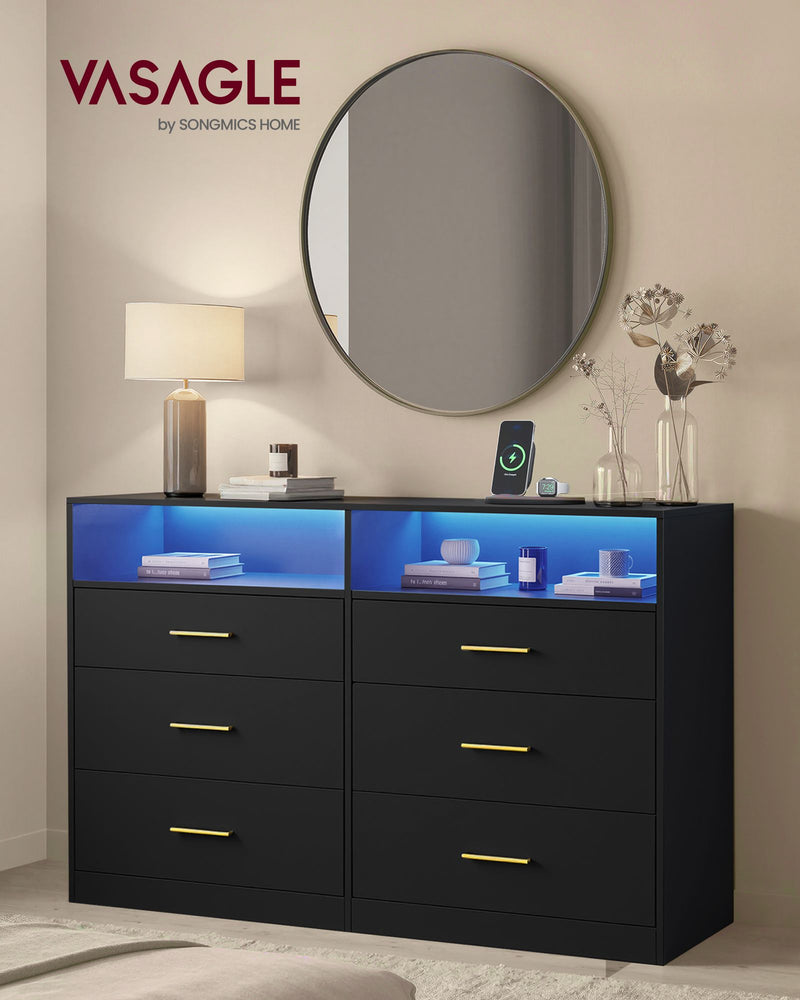 Black dresser with lit LED shelves in a bedroom beside a lamp and round mirror