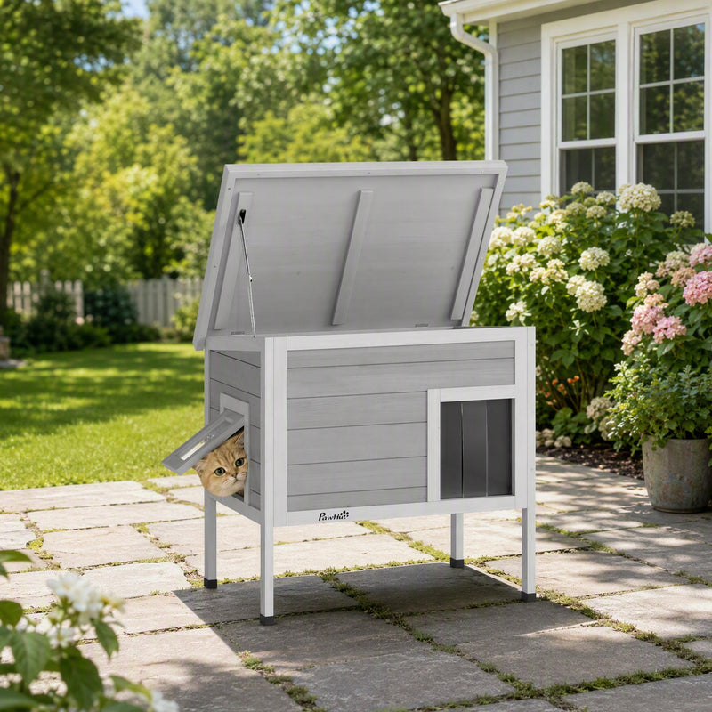 PawHut cat house with roof lifted open and a cat peeking out of the escape door in a garden