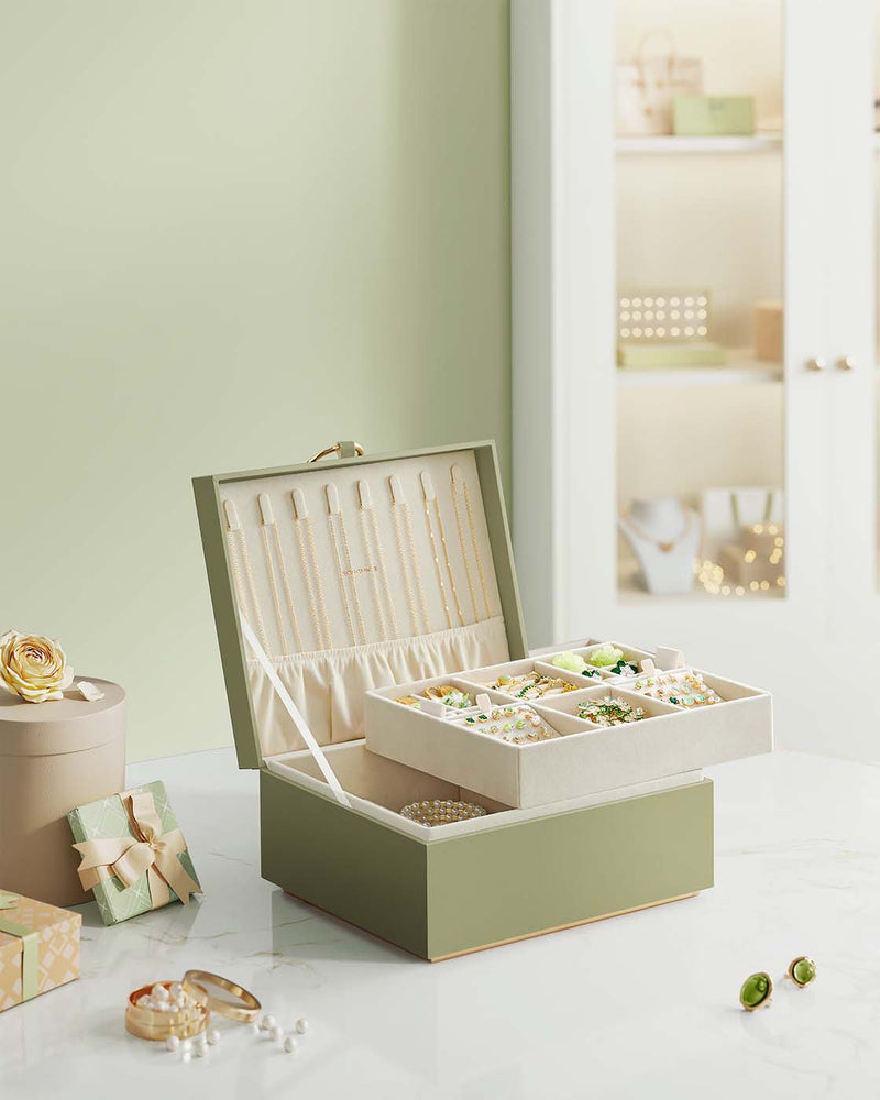 Light green jewellery box open on a dressing table surrounded by gift boxes and jewellery pieces