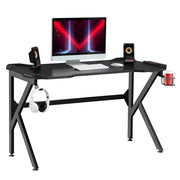 Black K-shaped gaming desk with a monitor, speakers, headphones on the hook and a red cup in the holder