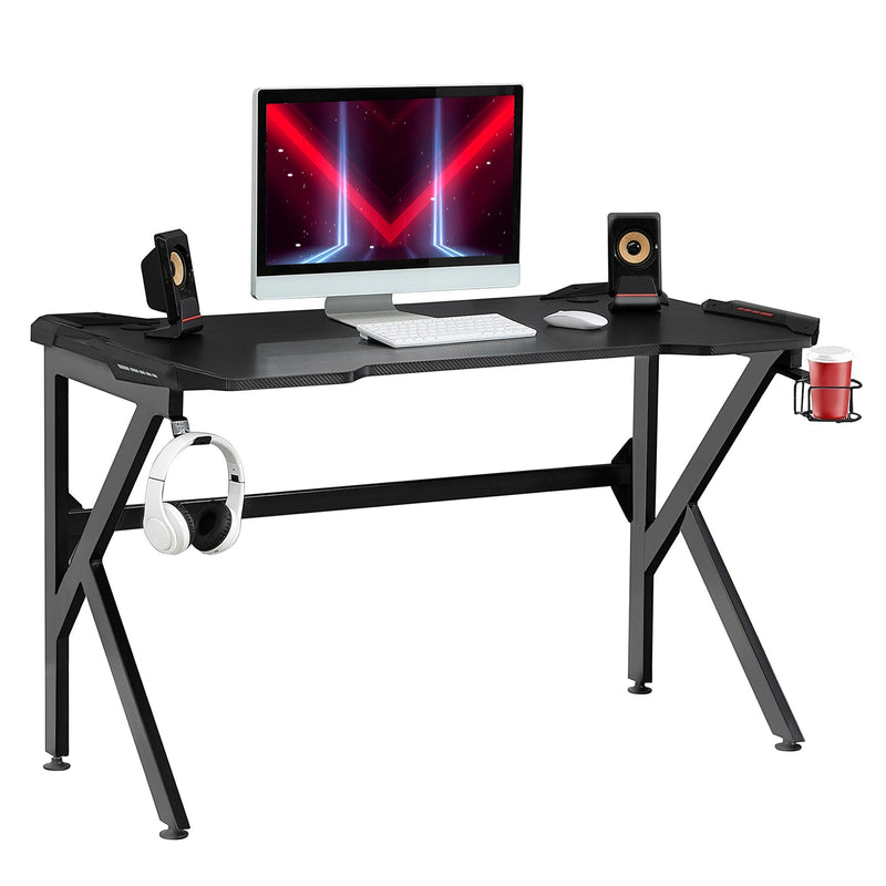 Black K-shaped gaming desk with a monitor, speakers, headphones on the hook and a red cup in the holder