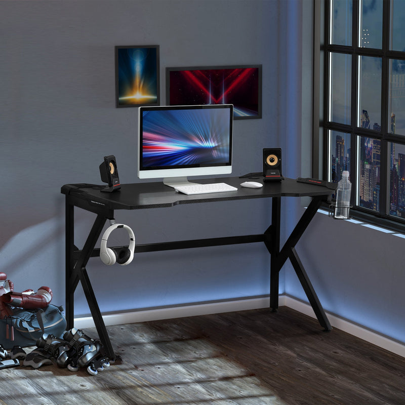 Gaming desk in a room corner by a window with a monitor, speakers and headphones on the hook