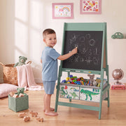 Boy drawing with chalk on the green kids easel chalkboard in a bedroom