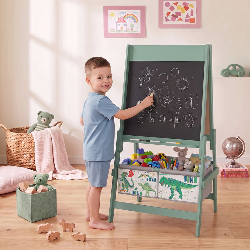 Boy drawing with chalk on the green kids easel chalkboard in a bedroom