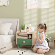 Child kneeling beside the green bedside table displaying books and framed pictures on top