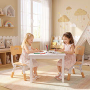 Two girls colouring at a table on kids chairs in a playroom with a play tent