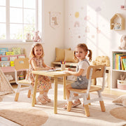 Two girls drawing at a wooden table on matching kids chairs beside a bookshelf