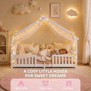 Child asleep in the white house bed frame decorated with fairy lights and plush toys