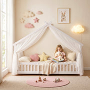 Child reading inside the white house bed frame with sheer canopy drapes