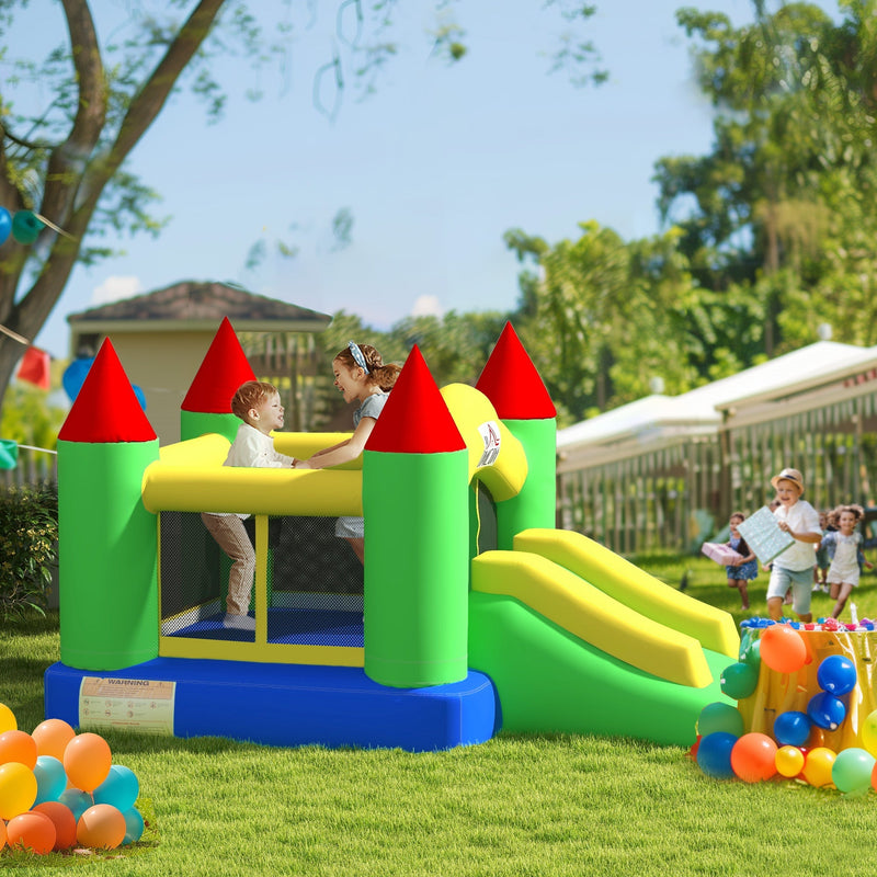 Green, yellow and blue bouncy castle on a lawn with children playing and balloons nearby