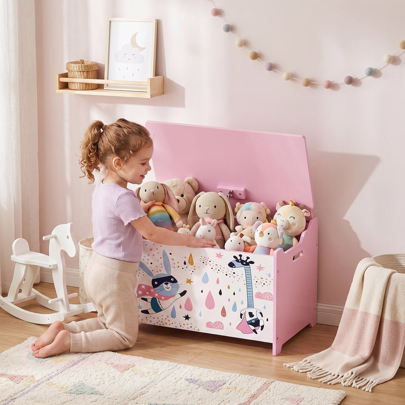 Child putting soft toys into the pink toy chest in a bedroom