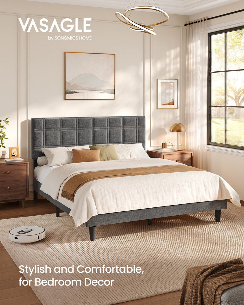 Slate grey upholstered king size bed in a sunlit bedroom with a robot vacuum beside the frame