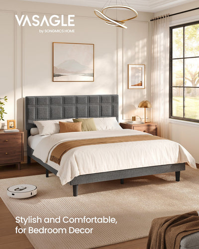 Slate grey upholstered king size bed in a sunlit bedroom with a robot vacuum beside the frame