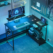 L shaped gaming desk with blue LED lighting in a bedroom corner with monitor, keyboard and laptop