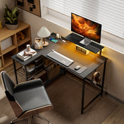 Black L shaped desk in a home office corner with warm lamp and a chair