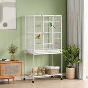 White bird cage with two birds in a green room, supplies stored on the bottom shelf