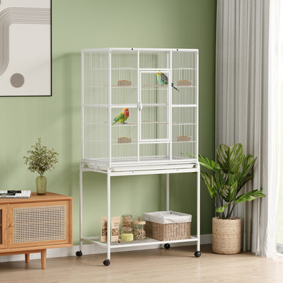 White bird cage with two birds in a green room, supplies stored on the bottom shelf