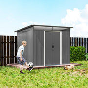 Grey metal shed on grass beside a dark fence with a child playing football nearby