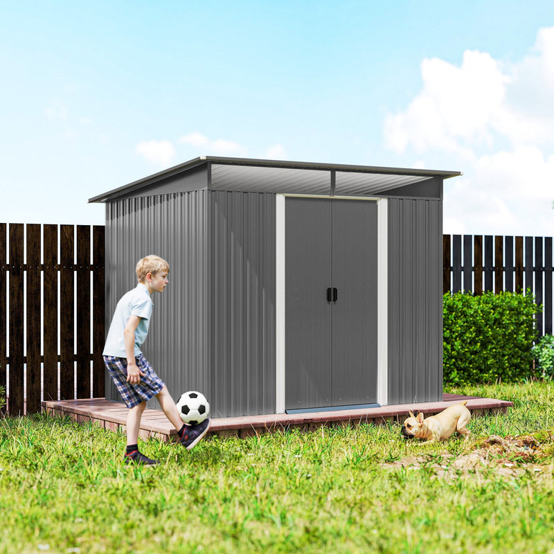 Grey metal shed on grass beside a dark fence with a child playing football nearby