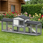 Rabbit hutch on a lawn beside a log cabin with a brown and white rabbit in the left run box