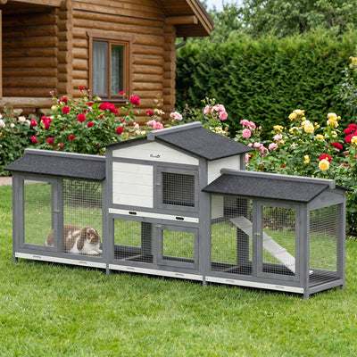 Rabbit hutch on a lawn beside a log cabin with a brown and white rabbit in the left run box