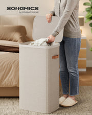 Person placing towel into Songmics laundry basket in a bedroom setting