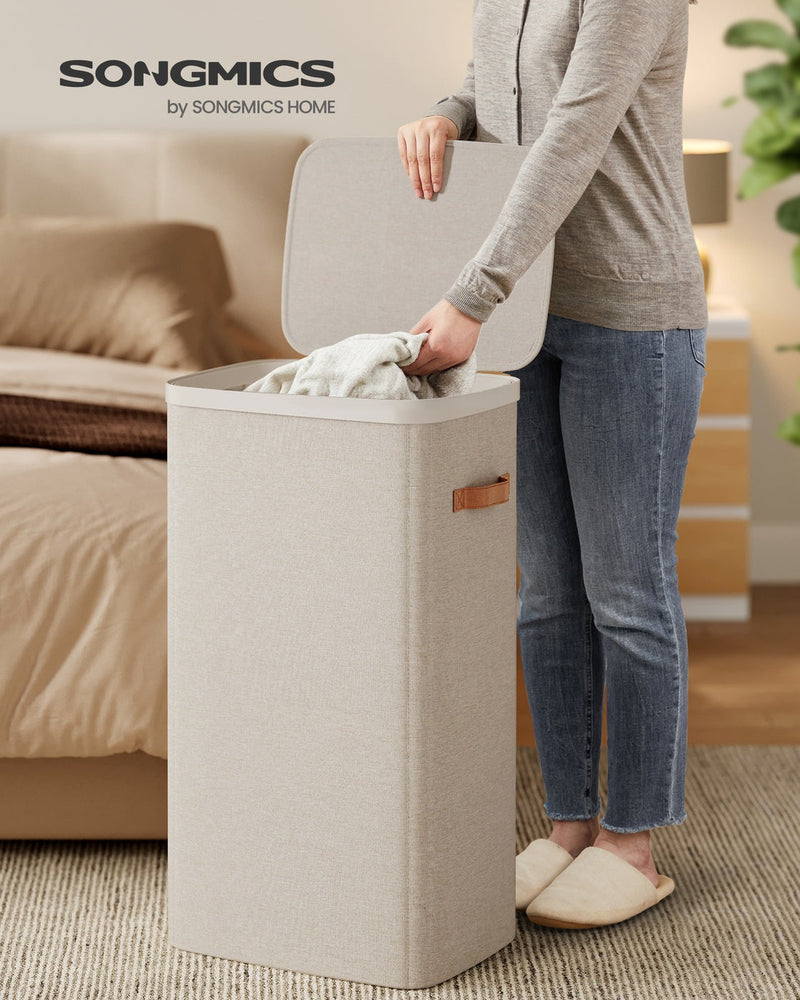 Person placing towel into Songmics laundry basket in a bedroom setting