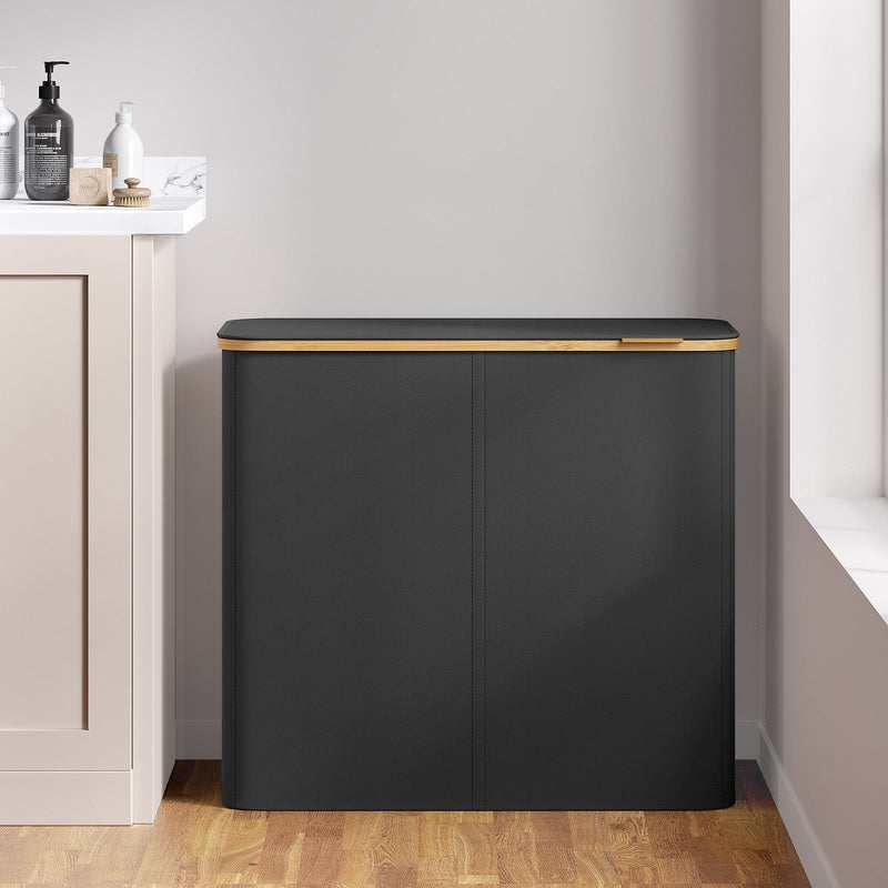 Closed black laundry hamper placed against a wall beside a bathroom vanity unit