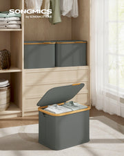 Two grey lidded baskets on a wardrobe shelf with one open showing folded clothes