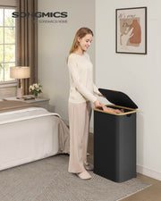 Woman placing folded clothes into the ink black laundry hamper in a bedroom