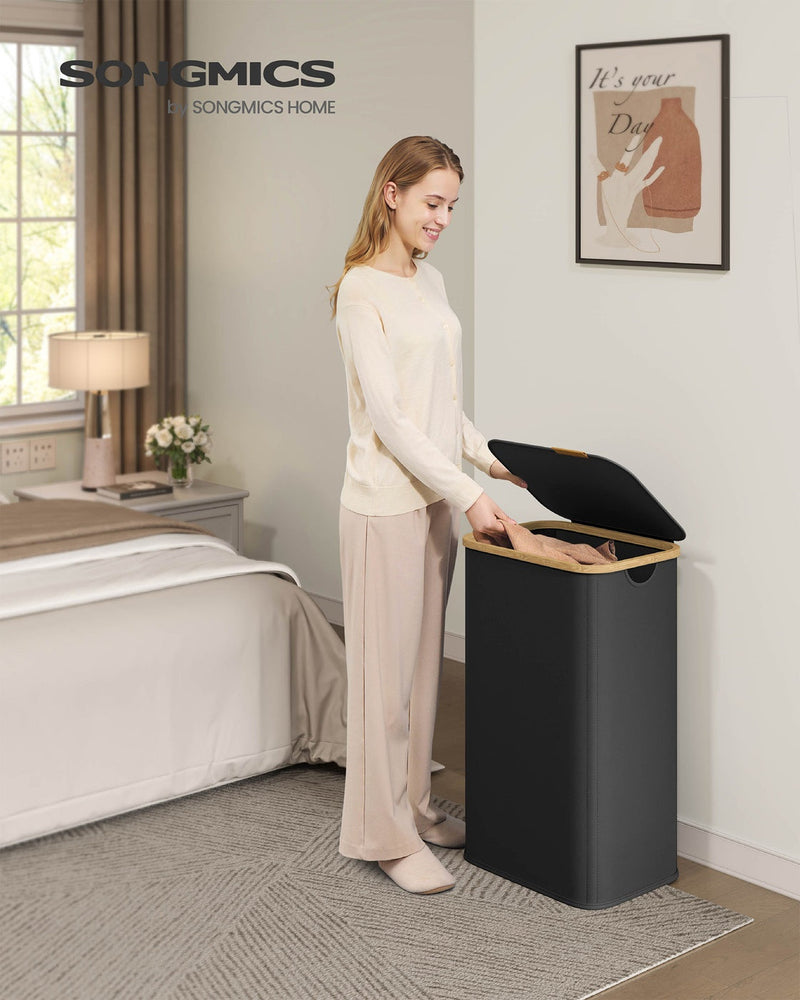 Woman placing folded clothes into the ink black laundry hamper in a bedroom