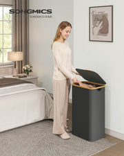 Woman placing folded clothes into the slate grey laundry hamper in a bedroom