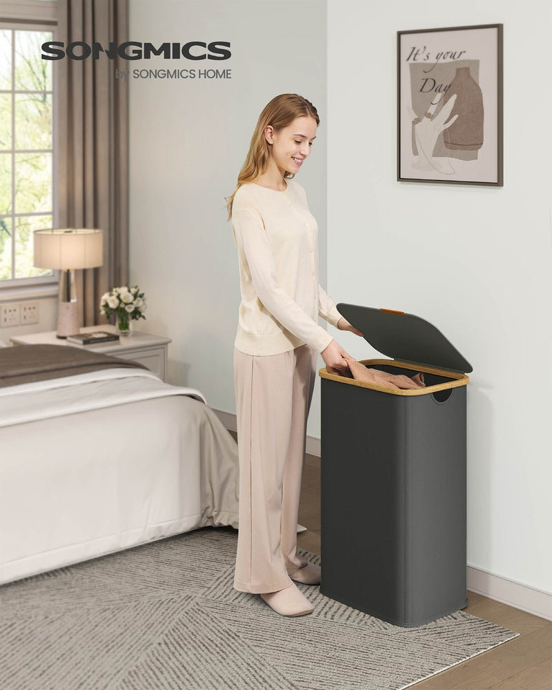 Woman placing folded clothes into the slate grey laundry hamper in a bedroom