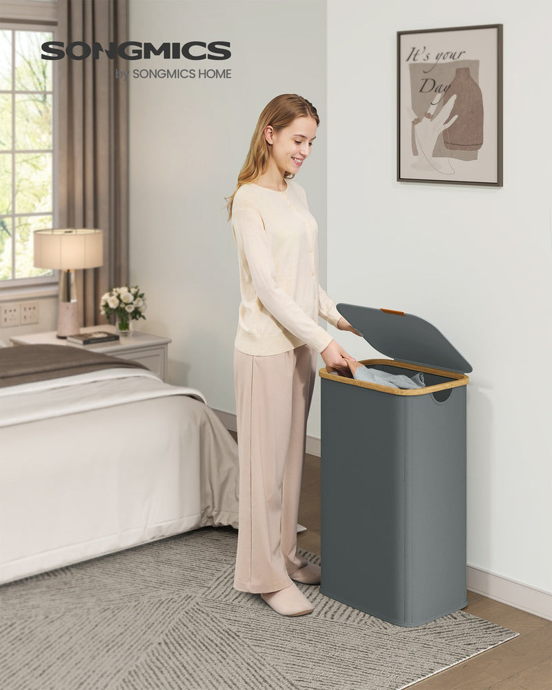 Slate grey laundry hamper styled beside a bed, shown from a different bedroom angle