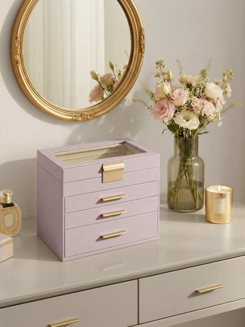 The jewellery box on a cream dresser below a round gold mirror, next to pink roses