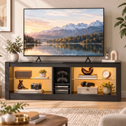 Black TV stand in a living room with warm LED lighting, a wall TV above and ornaments on the shelves