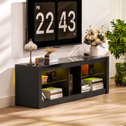 Black TV stand under a wall-mounted TV with a plant and books on the shelves