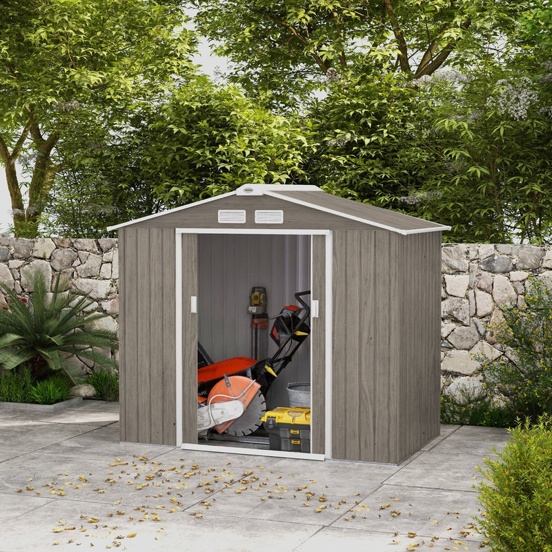 Light brown 7x4ft metal shed on a patio with the sliding doors open, showing garden machinery stored inside