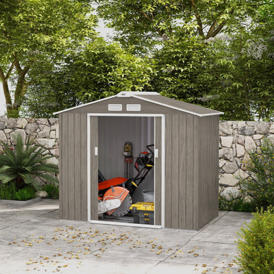 Light brown 7x4ft metal shed on a patio with the sliding doors open, showing garden machinery stored inside