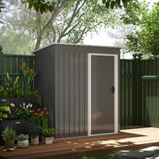The grey shed with its door closed, set on paving beside a dark green garden fence
