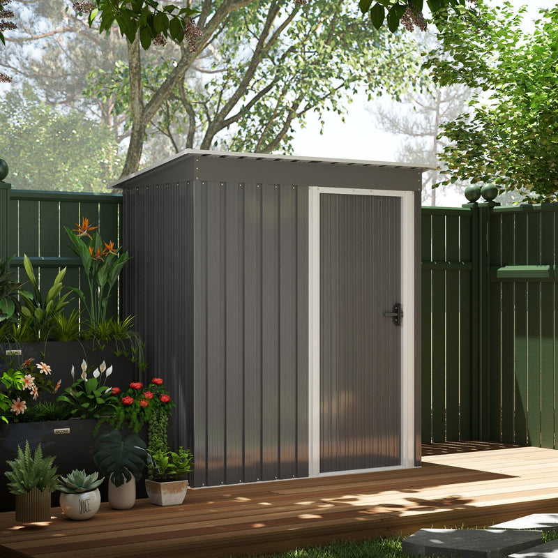The grey shed with its door closed, set on paving beside a dark green garden fence